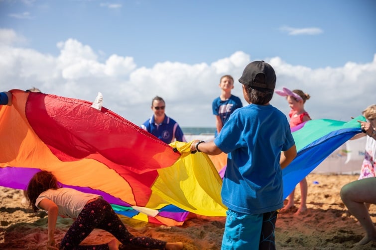 Festival of sails image of kids playing parachute on the beach. 