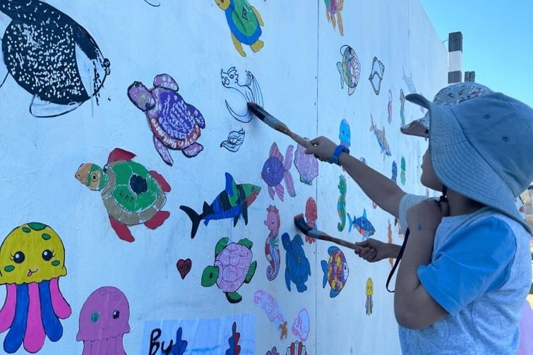 Brisbane Street Art Festival event image if girl painting on white wall with a paint brush.