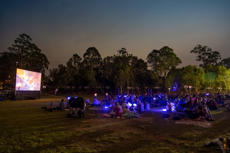 Movie in the park event image of people watching movie on the big screen at the park.