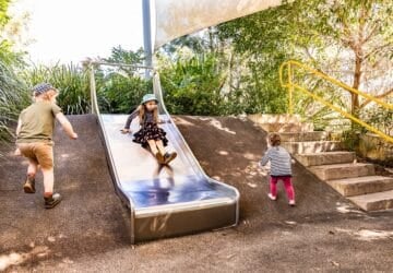 kids doing free school holiday activities in brisbane sliding down a metal slide set into a hill.