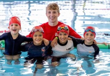 Griffith Sport smiling instructor with group of junior swimmers in pool.