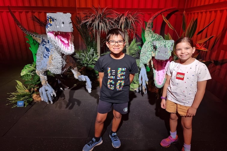 Two children posing with two velociraptors made of LEGO at Jurassic World by Brickman.