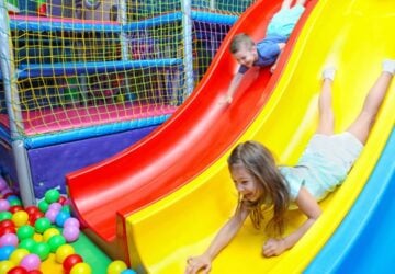 Two children sliding head first down slide into ball pit.