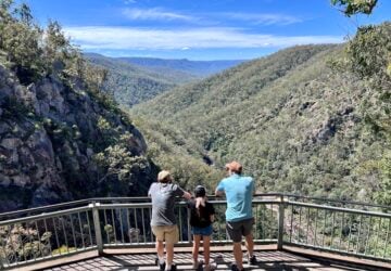 A family look out over a waterfall and deep gorge in Boonoo Boonoo National Park from a viewing platform.