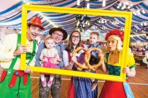 Oktoberfest image of family in traditional German clothing and a giant pretzel.