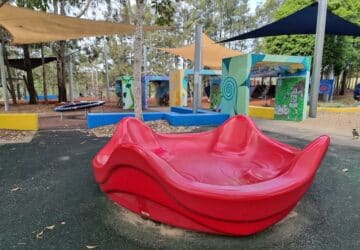 Red round-about and play equipment at Upper Kedron Park.