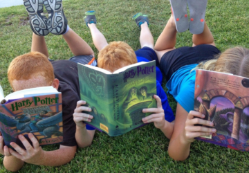 3 kids lying on the grass reading harry potter books.